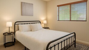 A bedroom with a bed, two bedside tables, a wall-mounted artwork, a window with blinds, and a patterned rug. - Desert Voyage | Pool | Near ASU + Old Town Scottsdale (Tempe)