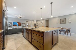 A modern kitchen with a central island, built-in appliances, pendant lighting, and a dining area with a table and chairs.