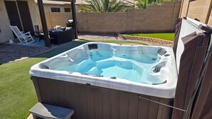 A hot tub with steps and a cover, surrounded by a patio area with a table and chairs.