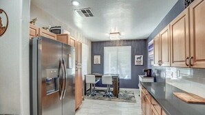 A compact kitchen with a refrigerator, wooden cabinets, a dining table with chairs, and a window.