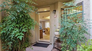 Une entrée abritée avec une porte donnant sur un espace intérieur, une petite table avec un pot de fleurs et un luminaire fixé au mur.