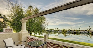 A balcony with a view of a lake, a chair, and a table.