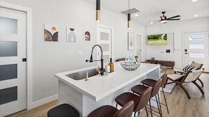 Eine moderne Küche mit Kochinsel, Barhocker, Pendelleuchten und Deckenventilator.