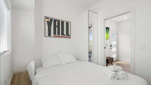 Ein modernes Hotelzimmer mit einem großen Bett, einem gerahmten Kunstwerk an der Wand und Blick auf den Flur.