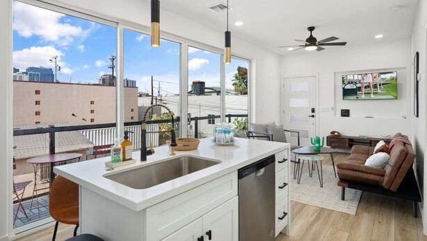 A modern kitchen with a large window, a dishwasher, and a dining area with a brown sofa and a small table. - Home Run! Walk to Chase Field | 2BR Summer Stay in Downtown PHX (Phoenix)