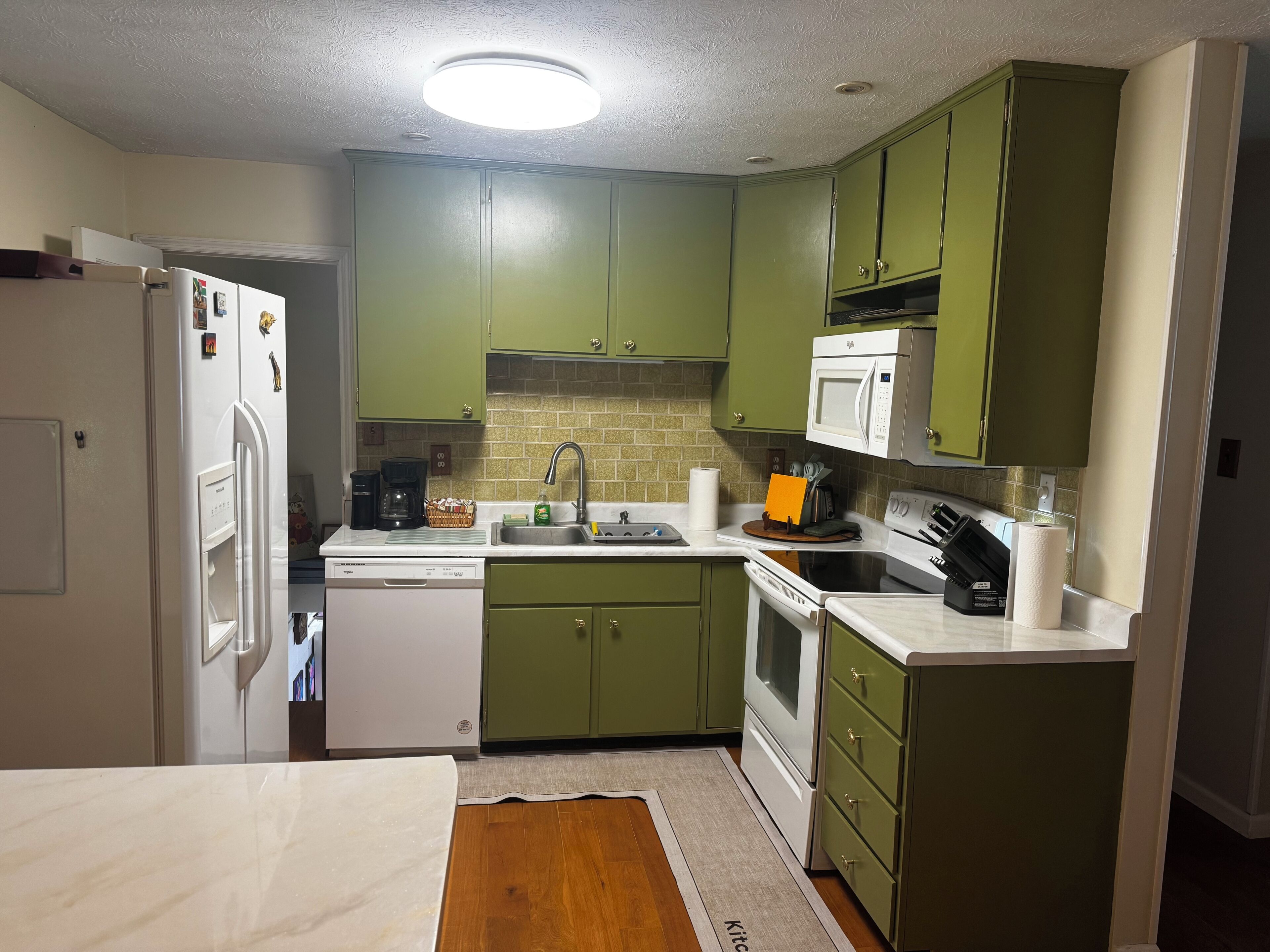 A kitchen with green cabinets, a white refrigerator, a microwave, a sink, and a stove.