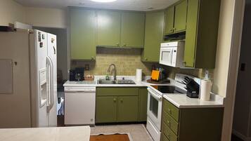 A kitchen with green cabinets, a white refrigerator, a microwave, a sink, and a stove.