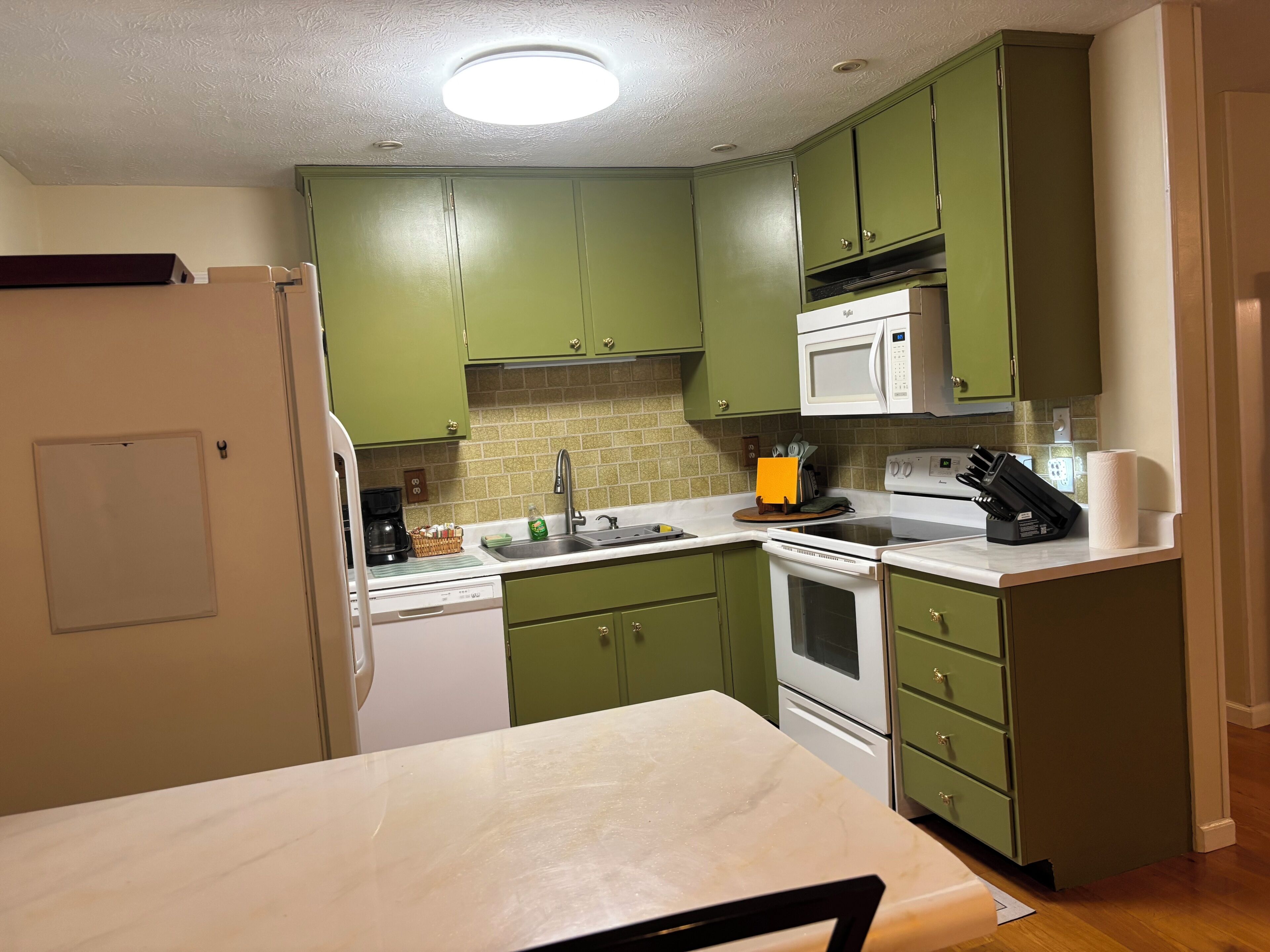 A kitchen with green cabinets, a white microwave, a sink, and a stove.