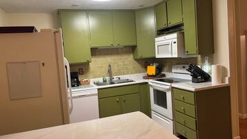 A kitchen with green cabinets, a white microwave, a sink, and a stove.