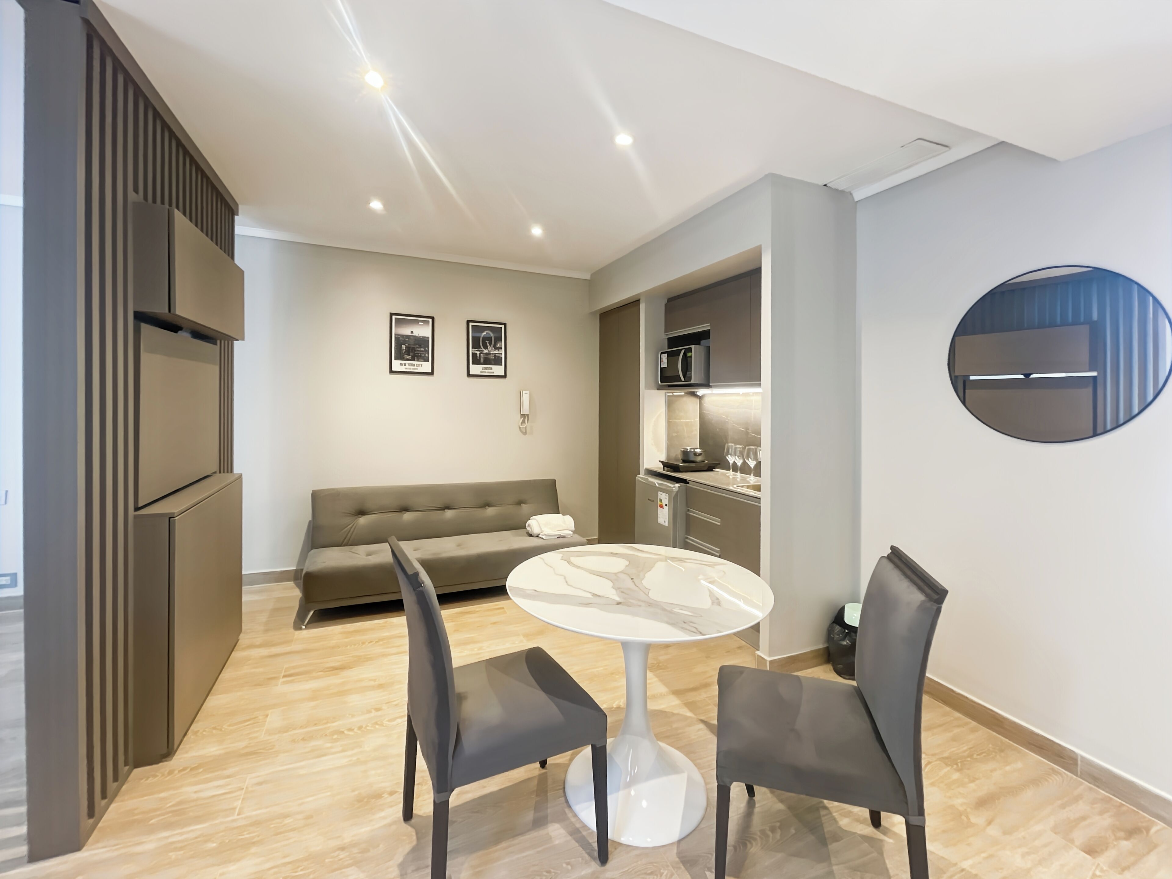 A modern living room with a sofa, two chairs, a round table, and a kitchen area with a microwave and refrigerator.