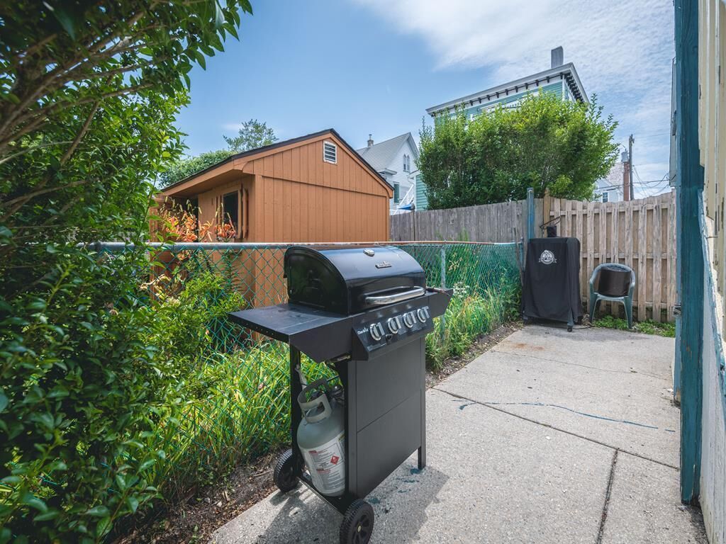 Un jardin avec un barbecue sur roulettes, un abri en bois et une clôture.