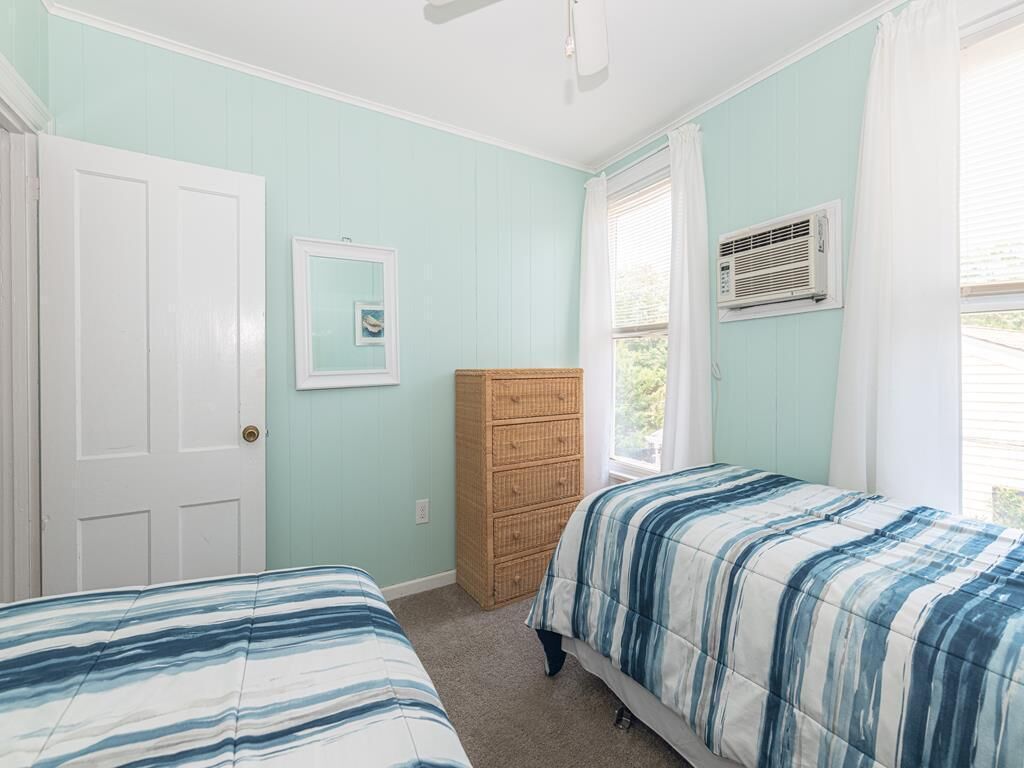 A bedroom with two beds, a dresser, a door, and a window with curtains.
