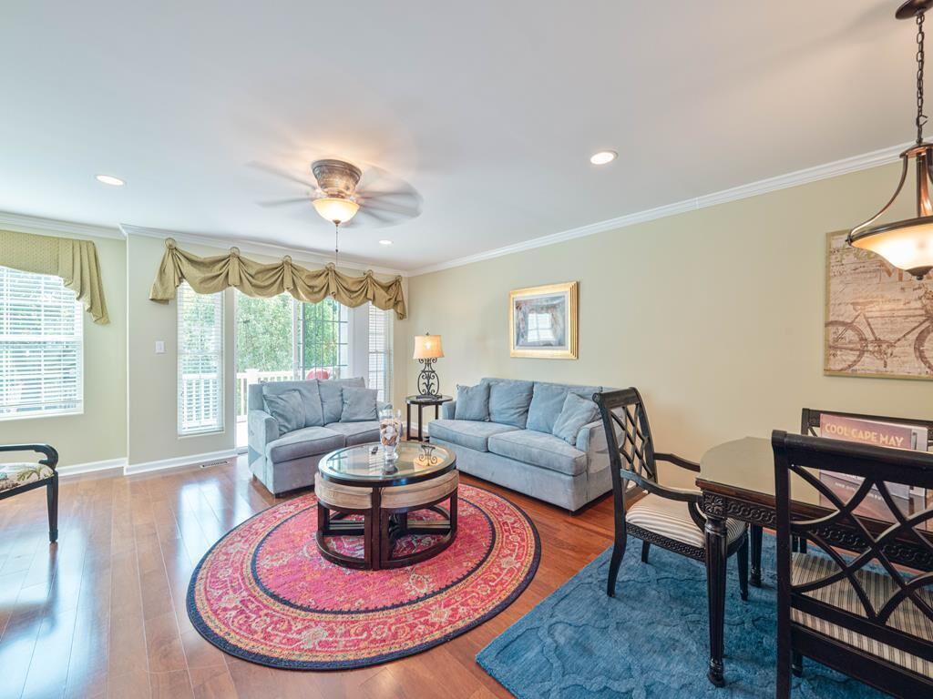 A living room with a round coffee table, two sofas, a dining table with chairs, a ceiling fan, and a large window with curtains.