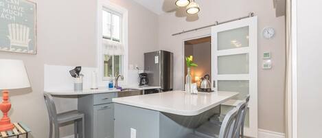 Una cocina moderna con armarios grises, una isla central, iluminación colgante y vistas al área de comedor.