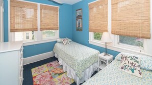 A bedroom with two beds, a ceiling fan, and large windows with bamboo blinds.