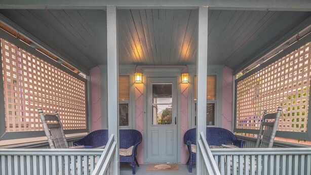 A porch with two wicker chairs, a door, and two wall-mounted lights.