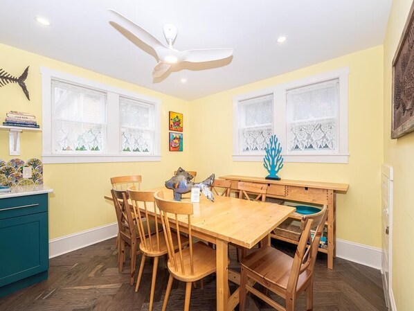A dining area with a wooden table and chairs, a ceiling fan, and decorative items on the walls.