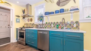 A kitchen with teal cabinets, a stainless steel dishwasher, and a tiled backsplash.