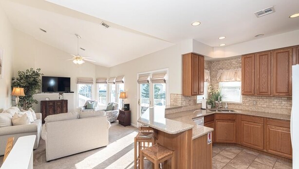A spacious living area with a kitchen and dining space, featuring a large island, wooden cabinets, and a flat-screen TV. - Top Floor Deck w/ Ocean View | Beach Block House (Cape May)