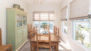 A dining area with a wooden table and chairs, a green cabinet, and large windows with blinds. - Top Floor Deck w/ Ocean View | Beach Block House (Cape May)