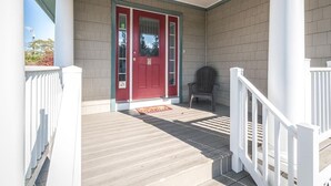 A covered porch with a red door, a white railing, and a grey chair. - Top Floor Deck w/ Ocean View | Beach Block House (Cape May)