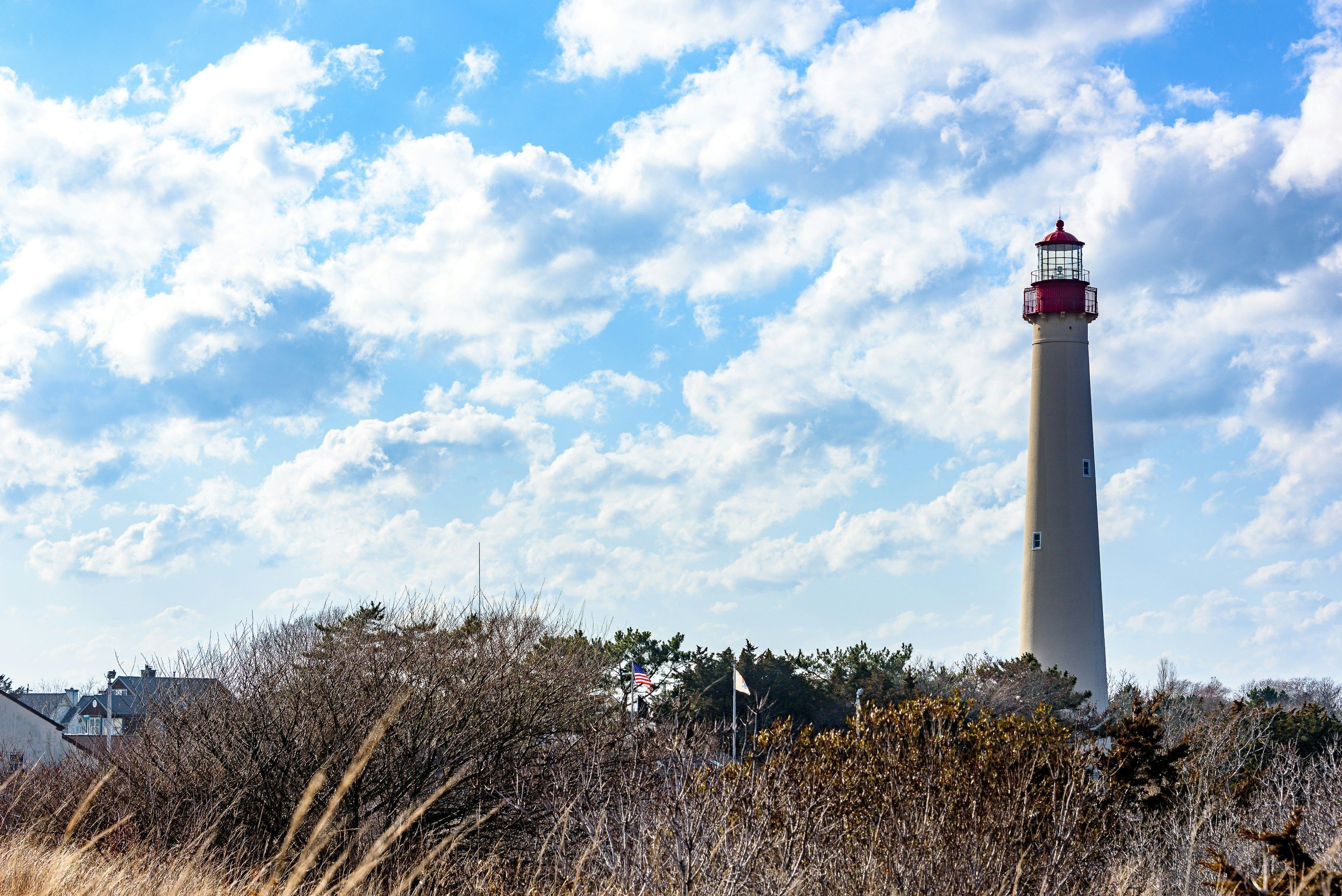 Un phare coiffé d’un dôme rouge, entouré d’une végétation aride et se dressant sous un ciel partiellement nuageux.