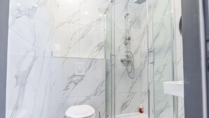 Un baño con ducha de vidrio, inodoro y pared con azulejos de mármol.