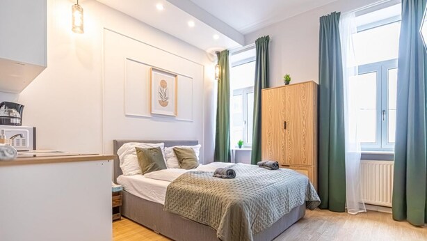 A bedroom with a bed, a wooden wardrobe, a radiator, and a window with curtains. - Cozy & Quiet Studio in Vienna’s 12th District (Vienna)