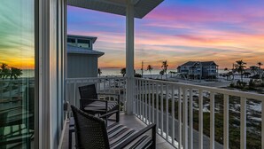 Un balcon avec deux fauteuils en osier et une vue sur la plage et le coucher de soleil.
