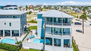 Une propriété en bord de mer, composée de plusieurs étages, dotée d’une piscine, d’un espace extérieur aménagé et offrant une vue sur la plage.