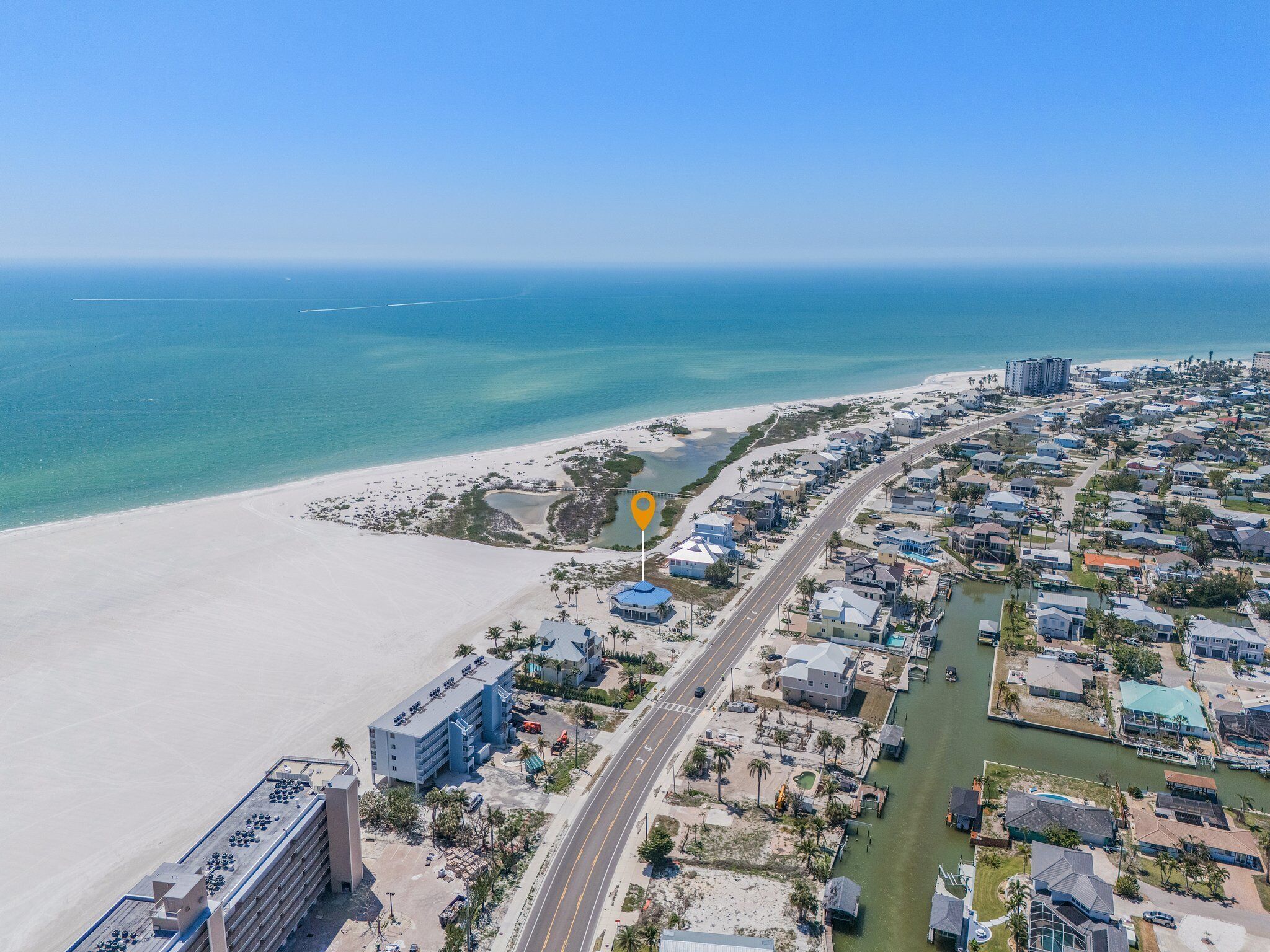 An aerial view of a coastal town with a beach, a marina, and a mix of residential and commercial buildings.