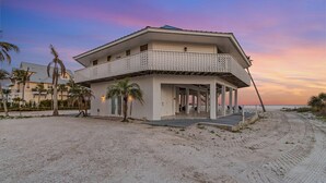 Ein Strandgrundstück mit einem zweistöckigen Gebäude, einem Balkon und einem Sandstrand im Vordergrund.