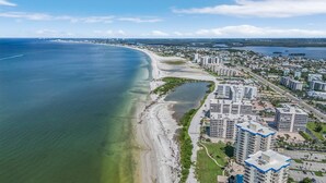 Ett flygbildsbild av en kuststad med en strand, bostadshus och en småbåtshamn.
