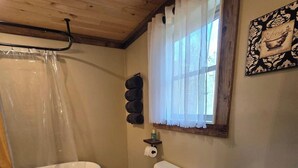 Un baño con bañera, inodoro y ventana con cortinas.
