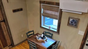 Un comedor con mesa de madera, cuatro sillas, una ventana con persianas y un equipo de aire acondicionado de pared.