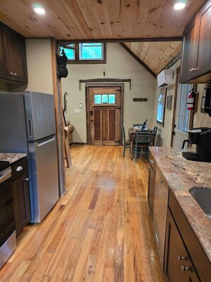 A kitchen with wooden flooring, a refrigerator, a coffee machine, and a dining area with chairs and a table.