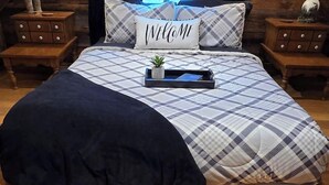Un dormitorio acogedor con colcha a cuadros, una almohada con la palabra 'Welcome' y una bandeja con un libro y una planta.