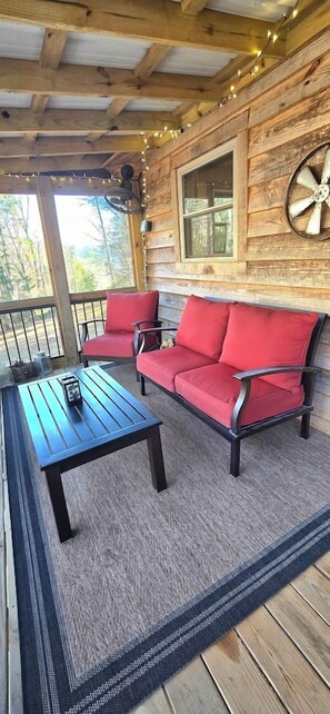 A wooden deck with a black table and red chairs, a window with a decorative wheel, and a string of lights.