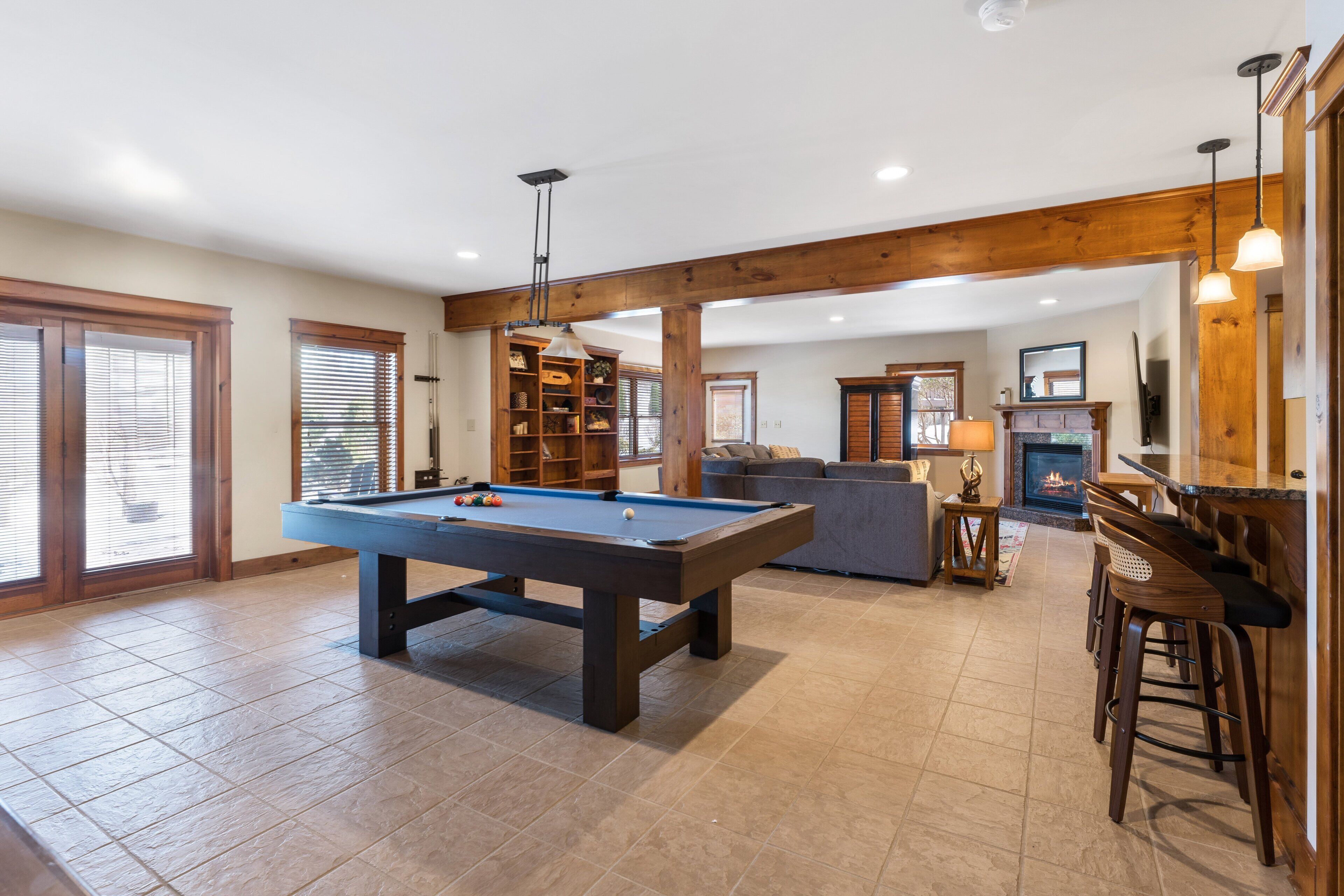 A pool table in a spacious living area with a fireplace, bar, and seating.