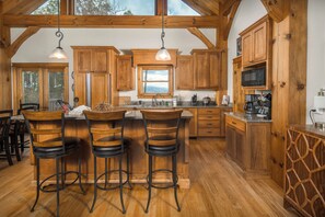 A spacious kitchen with wooden cabinets, a central island with bar stools, and a large window providing natural light.