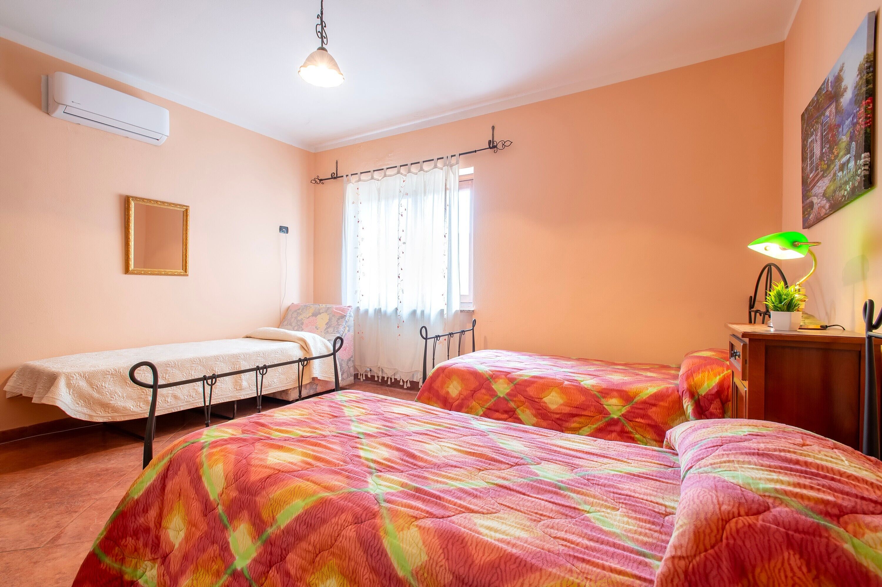 Una camera da letto con due letti, una finestra con tende, un comodino con una lampada e un condizionatore.