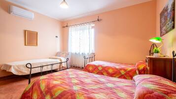 Una camera da letto con due letti, una finestra con tende, un comodino con una lampada e un condizionatore.