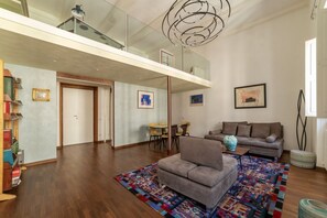 A modern living room with a grey sofa, a colorful rug, and a dining area with yellow chairs.