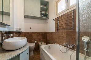 A bathroom with a large white sink, a toilet, a bidet, and a bathtub with a showerhead.