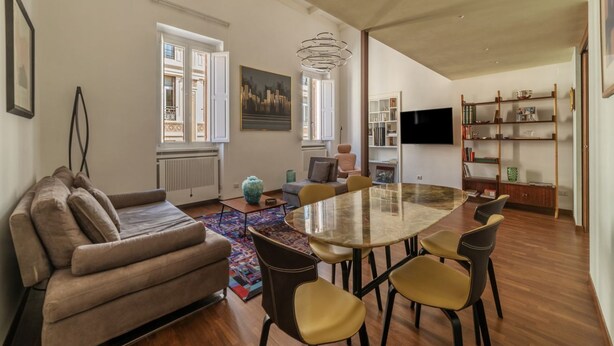 A modern living room with a sofa, dining table, chairs, a TV, and a bookshelf.