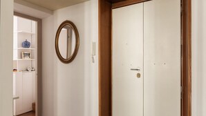 A hallway with a white wardrobe, a wooden floor, a wall-mounted mirror, and a shelf with decorative items.