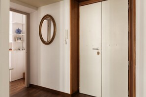 A hallway with a white wardrobe, a wooden floor, a wall-mounted mirror, and a shelf with decorative items.