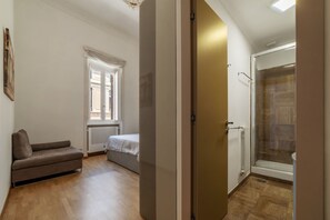 A bedroom with a bed, a sofa, and a shower area.