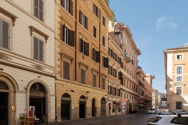 A street view of a row of historic buildings with arched windows and storefronts, including a pharmacy and a restaurant.