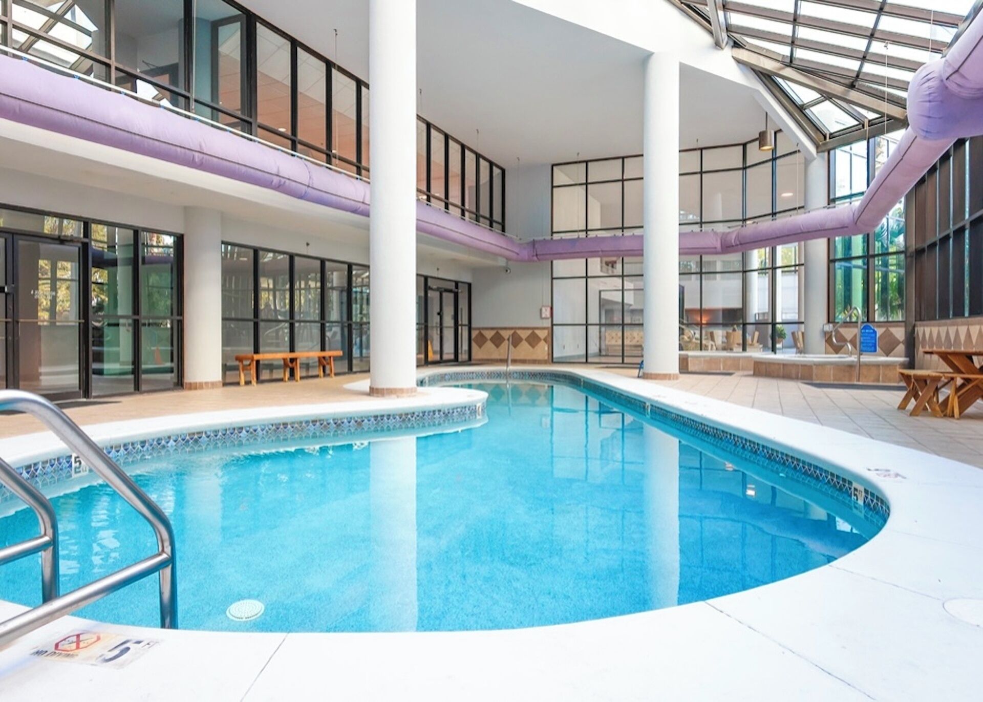 An indoor swimming pool with a clear view of the pool area, benches, and a glass ceiling.